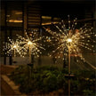 Decorative outdoor lights resembling fireworks on poles in a garden at night.