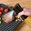 Person using a black oil sprayer on a grill with vegetables and meat.