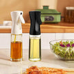 Two oil sprayers with different oils on a kitchen counter with a salad and shrimp in the background.