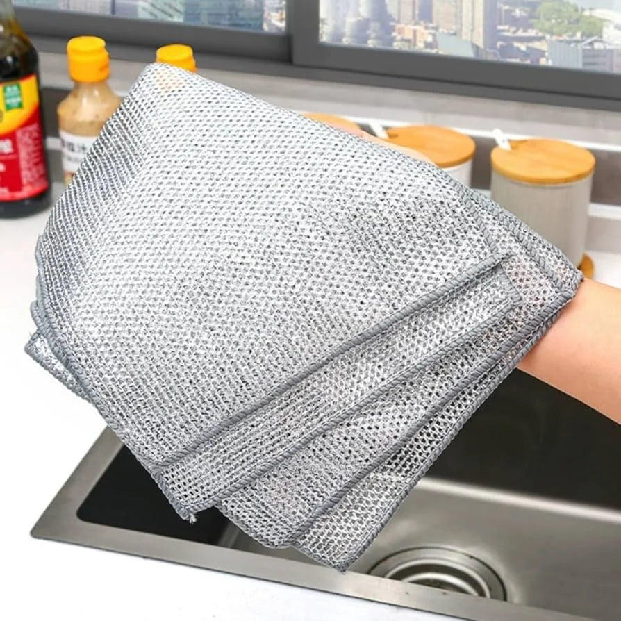 Metal mesh scrubber held over a kitchen sink with window view in the background