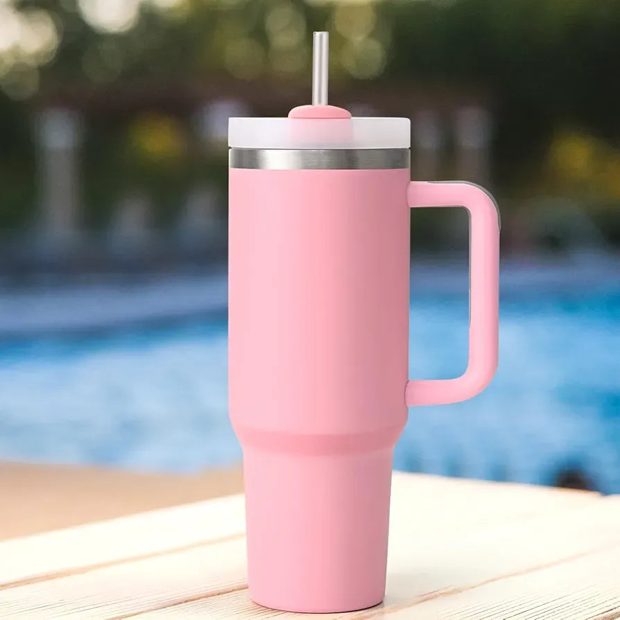 Pink insulated mug with handle and straw lid on a wooden surface by a pool.