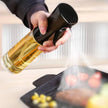 Hand holding a bottle of oil over a frying pan with food.