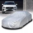 White car covered with a car cover in front of a gray building.