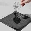 Glass of water being poured onto a black mat with a white background