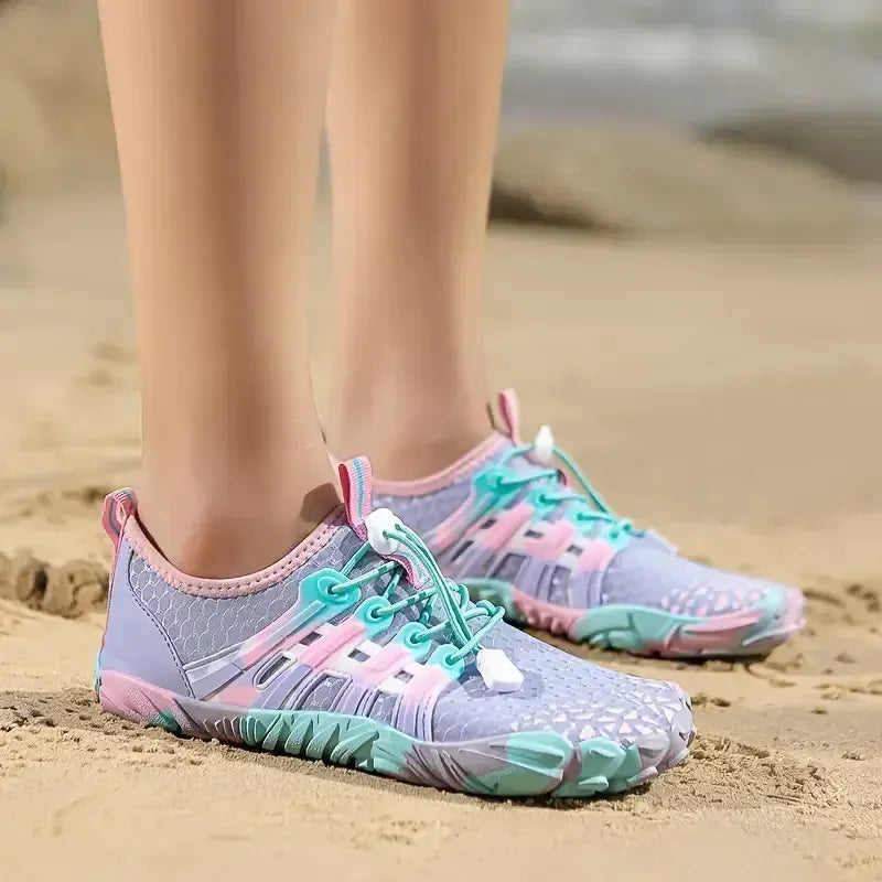 Purple and pink water shoes with blue accents on a sandy beach.