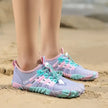 Purple and pink water shoes with blue accents on a sandy beach.