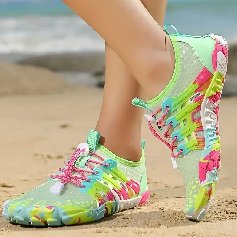 Colorful water shoes on a sandy beach with ocean in the background