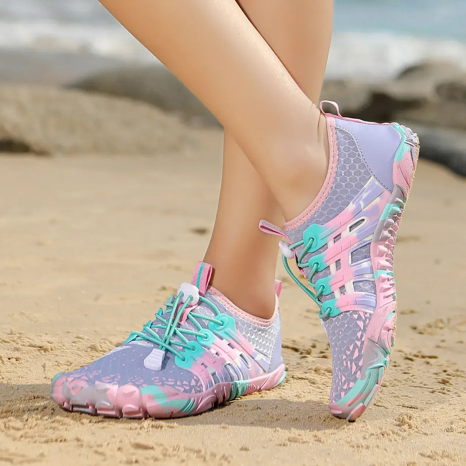 Pastel-colored water shoes on a beach with blurred ocean background