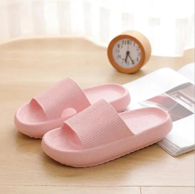 Pink slippers on a wooden surface with a clock and book in the background