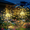 Two solar-powered outdoor lights resembling fireworks in a garden setting.