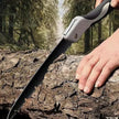 Hand using a folding saw on a log with a forest background