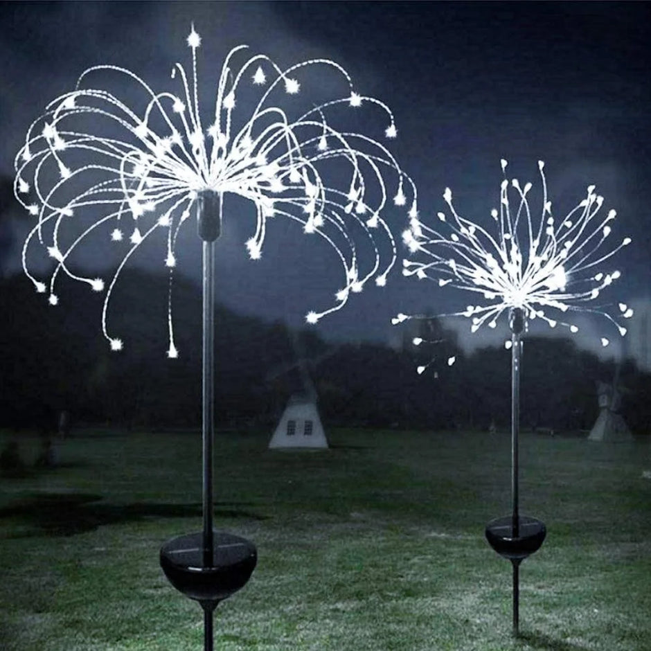 Two decorative solar lights shaped like fireworks on grass at night.