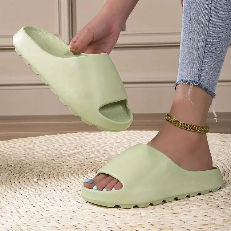 Person wearing a light green slide sandal on a textured floor.
