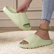 Person wearing a light green slide sandal on a textured floor.