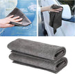 Gray microfiber towel being used to clean a car window and a car's exterior, with folded towels on a white background.