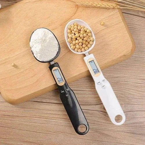 Two digital measuring spoons filled with flour and beans on a wooden surface.