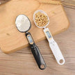 Two digital measuring spoons filled with flour and beans on a wooden surface.