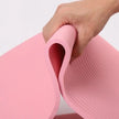Pink yoga mat being held by a hand on a light gray background