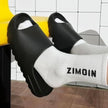 Person wearing black slides and white socks with 'ZIMOIN' branding in a bathroom setting.