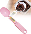 Pink digital measuring spoon with a bowl of coffee beans on a white background