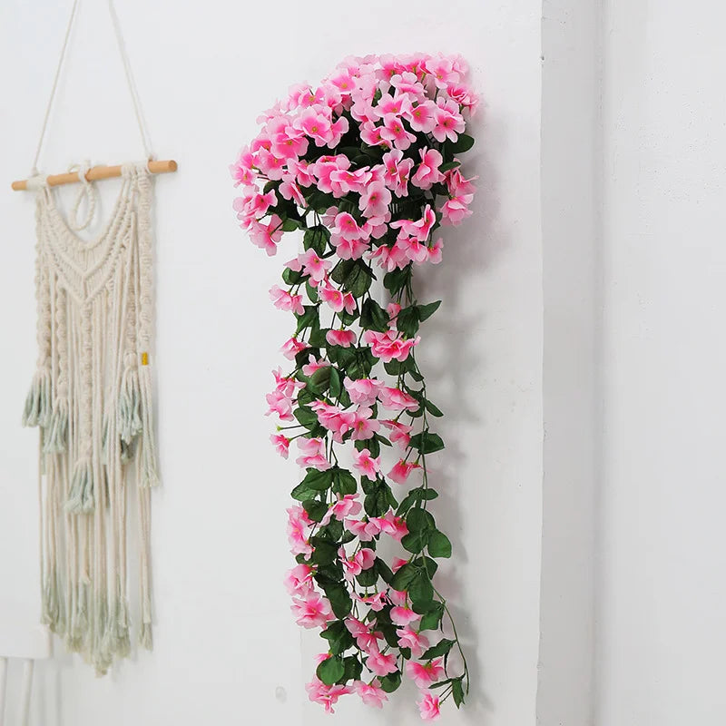 Artificial pink flower garland hanging on a white wall next to a macrame wall hanging.