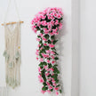 Artificial pink flower garland hanging on a white wall next to a macrame wall hanging.