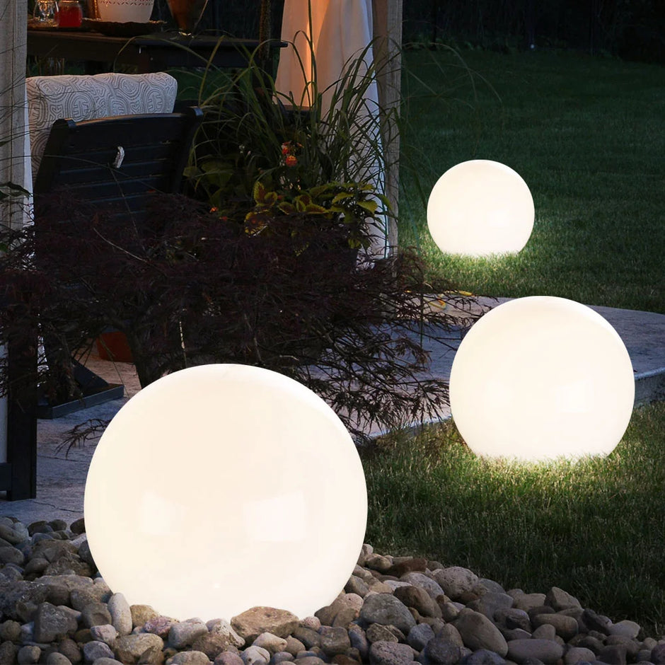 Three spherical outdoor lights on a garden path with plants and a bench in the background.